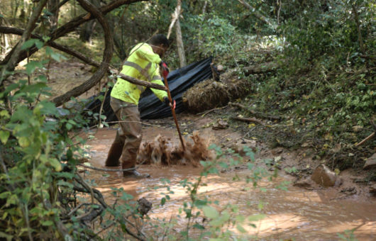 A cleanup worker attempts to rake mud upstream to a pumping pool. Photo by The Downstream Project